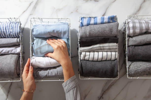 Neatly folded clothes and pyjamas in the metal mesh organizer basket on white marble table. modern style of garments declutter and sorting concept. Housewife using modern method of tidying up.
